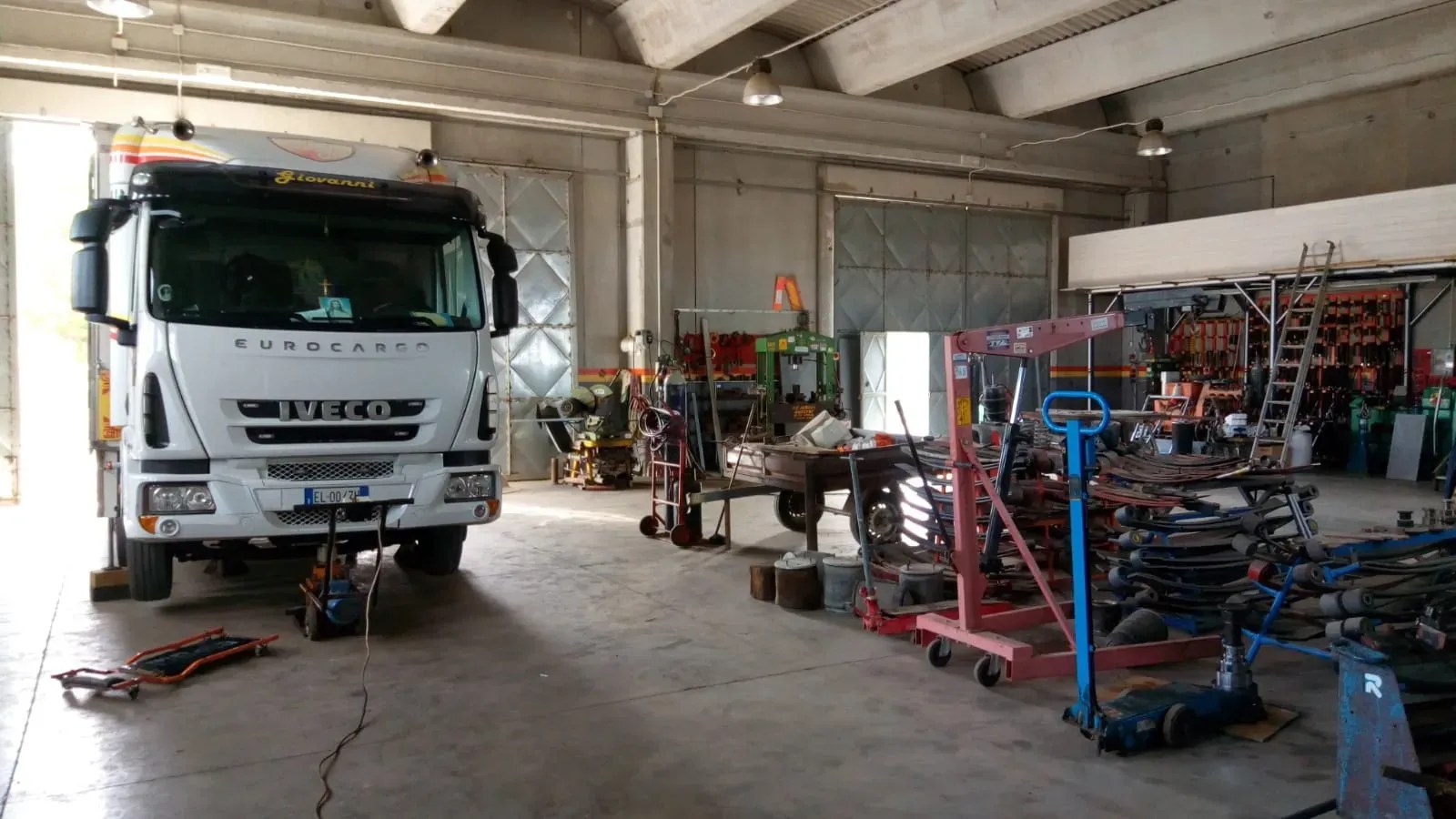 Interno dell'officina: un autocarro sollevato sul ponte, con le molle a balestra sulle rastrelliere.